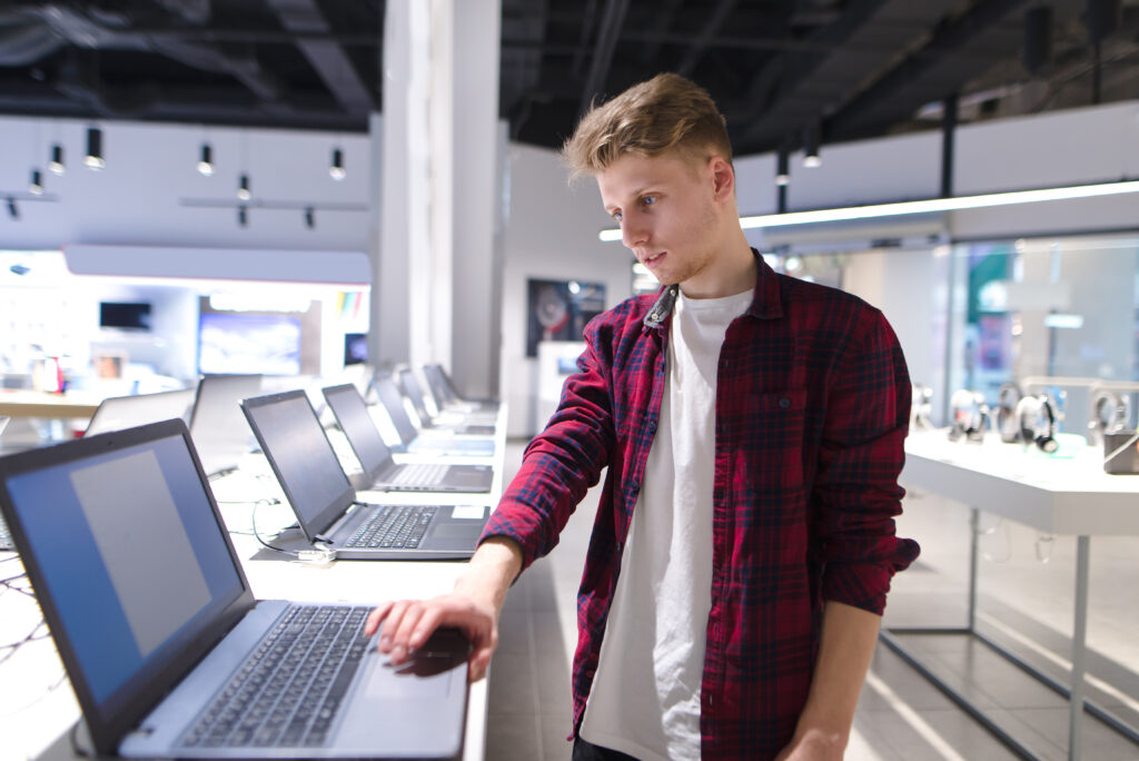 A young buyer chooses a laptop in a modern electronics store. A man buys a laptop in a technology store. Buy Gadget